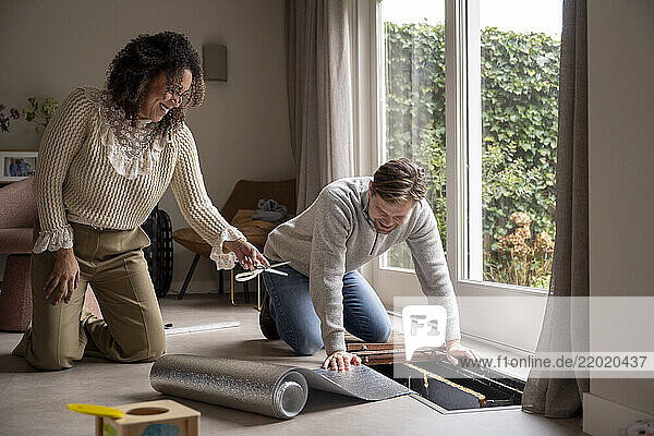 Man kneels installing flooring and isolation while woman assists in a bright  modern living room. Netherlands
