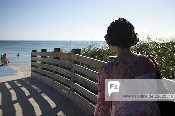 Woman in sunglasses walking on a beach boardwalk towards the ocean under a clear sky  Florida Keys  USA