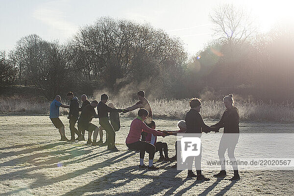 A group of people exercises outdoors on a frosty morning  holding hands in a line  while surrounded by trees. Sale Water Park  Manchester  UK