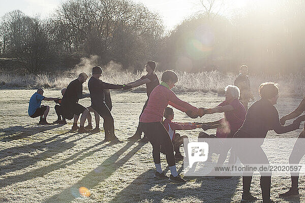 A group of adults engage in a team exercise in a frosty park on a sunny morning  creating a chain through linked arms. Sale Water Park  Manchester  UK