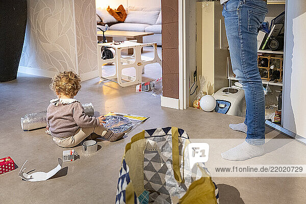 Young child with curly hair plays on the floor surrounded by household items indoors. Netherlands