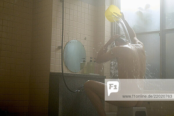 A man pouring water over himself with a yellow bucket in a tiled bathroom in a Japanese spa  Japanese Alps  Shiba Onsen
