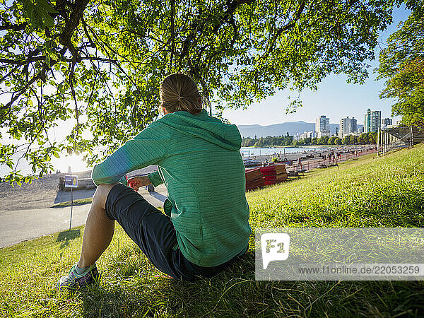 Rear view of woman sitting on lawn near coast