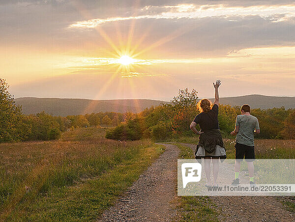 Rear view of mother and son (16-17) standing on dirt road in landscape at sunset