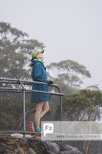 Female hiker in jacket and baseball cap standing on observation point