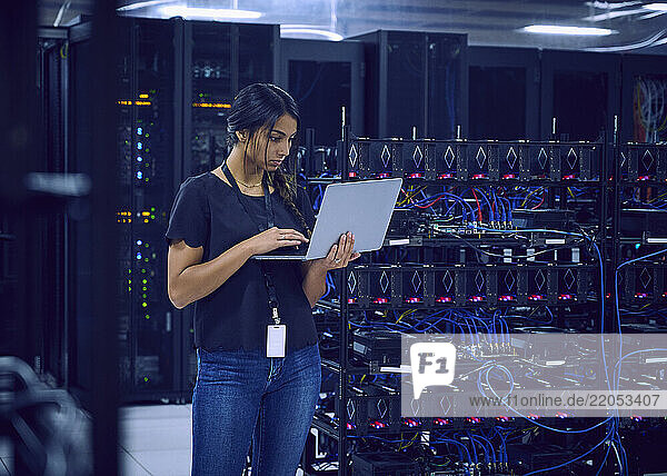 Female technician using laptop in server room