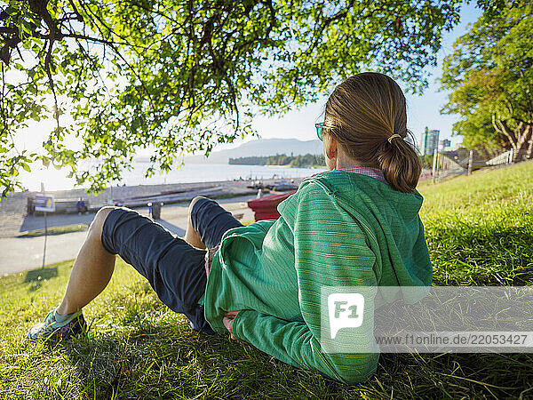 Rear view of woman sitting on lawn near coast