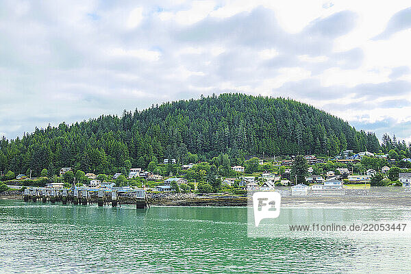 Pier and town with forested hill in background seen across water