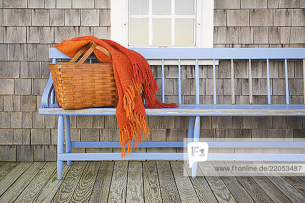 Picnic basket and orange blanket on blue wooden bench outside cottage house