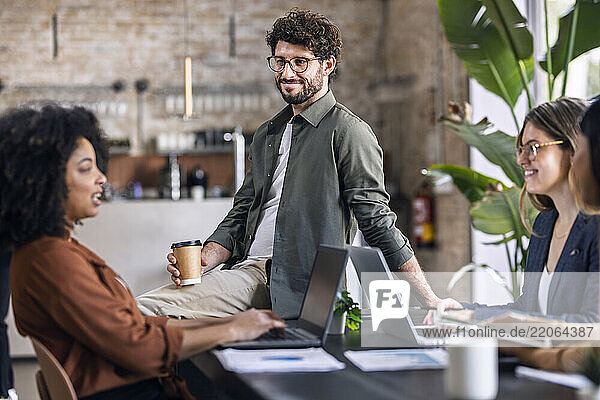 Smiling businessman sitting on table and talking with colleagues in office