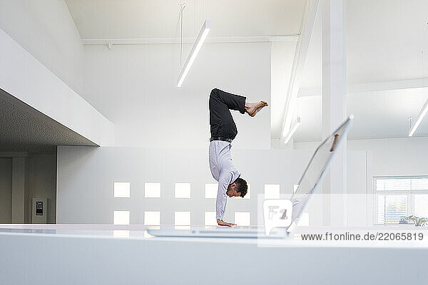 Businessman doing a handstand at laptop in office
