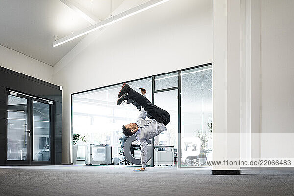 Businessman with cell phone doing a one-handed handstand on office floor