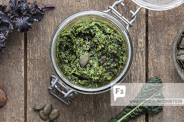 Jar of kale pesto with pumpkin seeds on a rustic wooden table