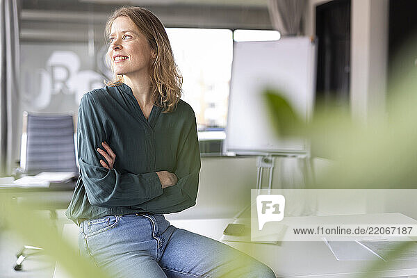 Thoughtful blond businesswoman sitting with arms crossed in office