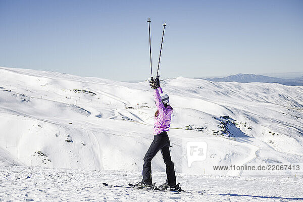 Happy woman raising her ski poles in snow-covered landscape in Sierra Nevada  Andalusia  Spain