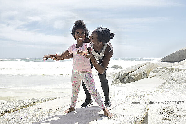 Mother and daughter doing a gymnastic exercise on the beach