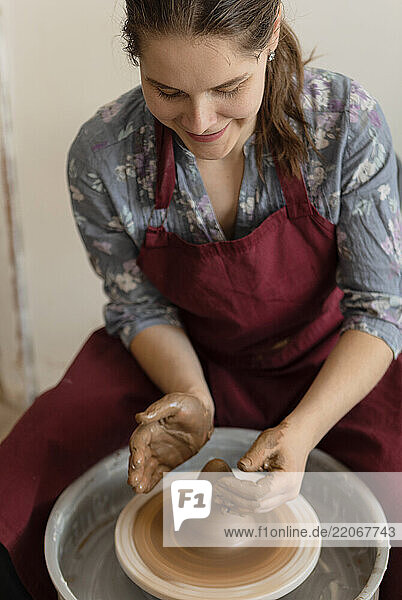 Smiling woman molding clay on pottery wheel in ceramics studio