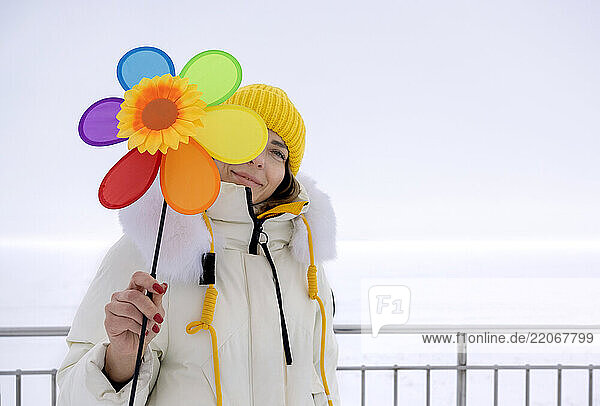 Woman holding a colorful flower in front of her face outdoors in winter
