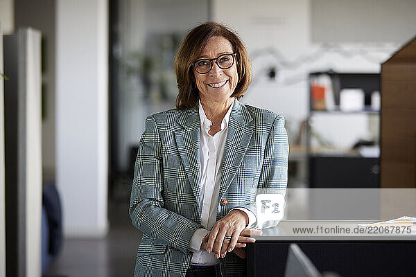 Smiling senior entrepreneur standing at desk in office