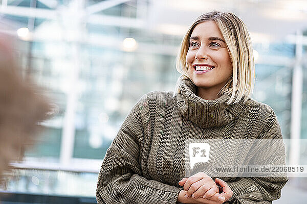 Young woman in a sweater smiling indoors in a modern urban setting