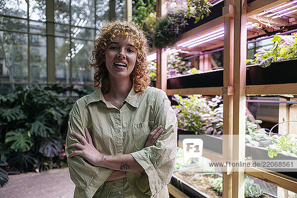 Happy redhead woman standing with arms crossed in garden center