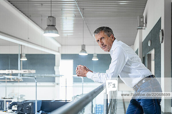 Confident businessman leaning on railing at factory