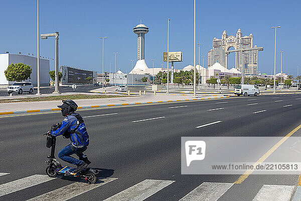 United Arab Emirates  Abu Dhabi. A man sitting on an electric scooter  with the Marina Mall and the Rixos Marina Abu Dhabi hotel in the background.