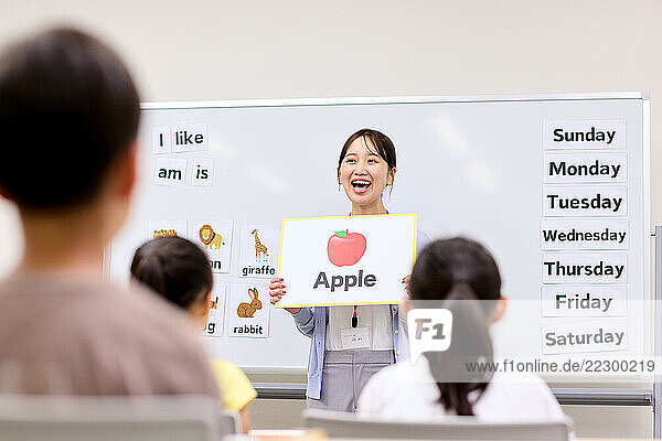 Japanese Woman Holding Up An Apple Sign In Front Of A Classroom