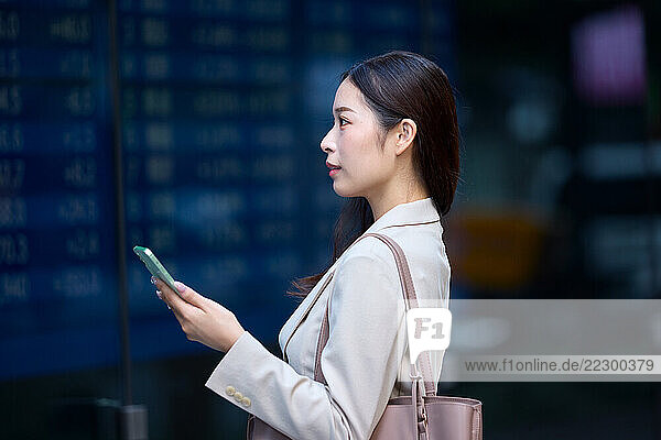 Japanese Woman Using Her Mobile Phone In Front Of A Stock ExcAnge Board