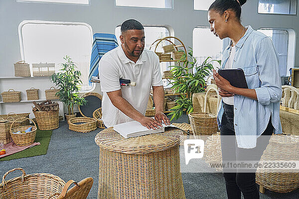 Two employees standing and talking in crafts shop with wicker furniture