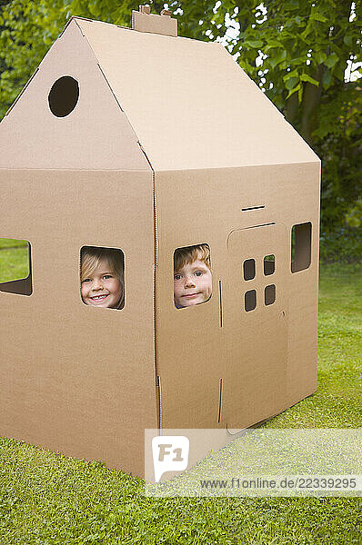 Boy and girl looking out from the windows of a cardboard playhouse