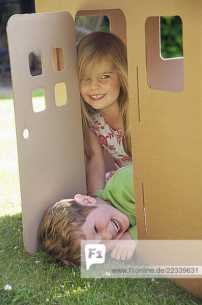 Boy and girl smiling in the doorway of a cardboard playhouse