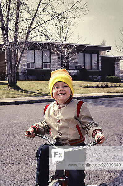 Portrait cute boy in stocking cap riding tricycle in sunny street outside house