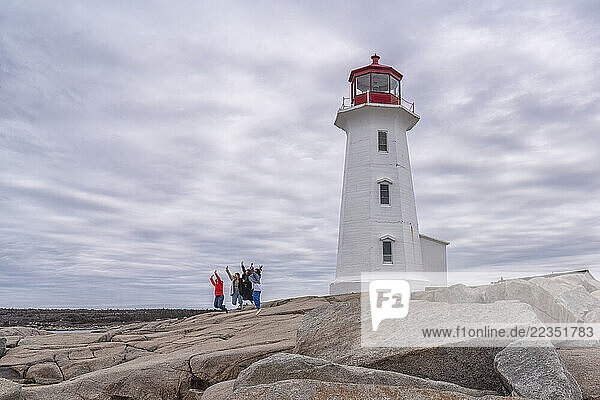 Group of people jumping in front of Peggy s Cove lighthouse on a cloudy morning; Peggy s Cove  Nova Scotia  Canada