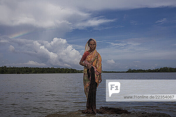Woman catch fish in the river in front of her house at the Kalabogi village in Khulna  Bangladesh  on 04 September 2023. In the coastal areas of Southern Bangladesh like Kalabogi  people‘s livelihoods depend entirely on nature. Climate change has severe impacts on the natural environment. The consequences range from rising sea levels leading to salinization of soils and groundwater to erratic rainfall patterns and more frequent and destructive tropical cyclones. People living in coastal areas fight for their survival every day; Khulna  Dhaka  Bangladesh
