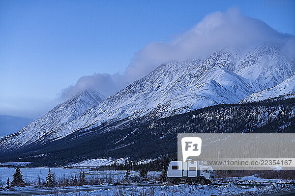 Recreation vehicle parked along the roadside on a Yukon Spring morning with Wallace and Sheep mountains in the background. The blue light of dawn is present with moody clouds enveloping the summit of both mountains; Yukon  Canada