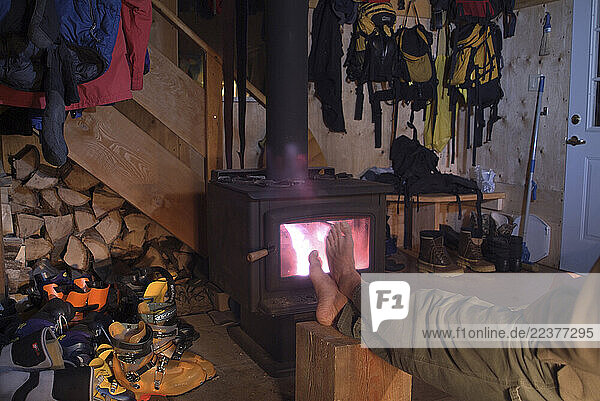 Warming frozen toes by the wood stove fire after a day of alpine touring in the back country of Sol Mountain  in British Columbia s Selkirk Mountain range.