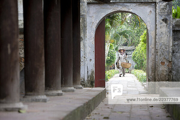 Hanoi  Vietnam - A grounds worker walks the path through an arched doorway at Quoc Tu Giam (National University) opened in 1076 under the Ly dynasty. Studies focused upon literature and poetry  with attention to the Four Books (The Great Study  The Golden Means  The Analects  Mencius); the Five Pre-Confucian Classics and other ancient poetry and Chinese history.