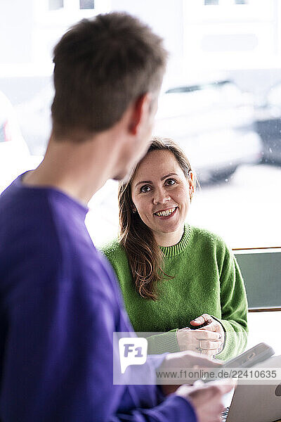 Woman in green sweater smiling at man in café while working on smartphone
