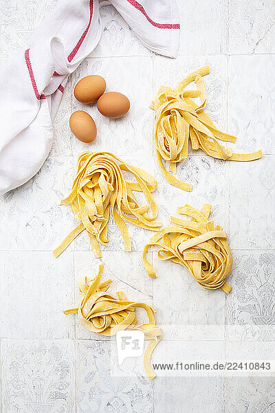 Fresh homemade pappardelle pasta with eggs and a kitchen towel on tiles