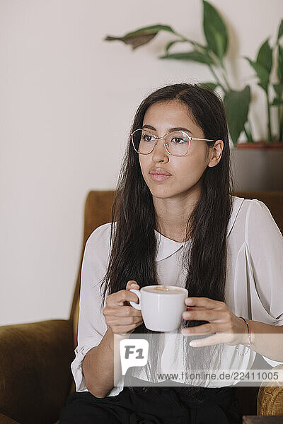 Young woman with cup of coffee sitting in armchair in a cafe