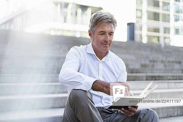 Mature businessman sitting on stairs looking at notebook