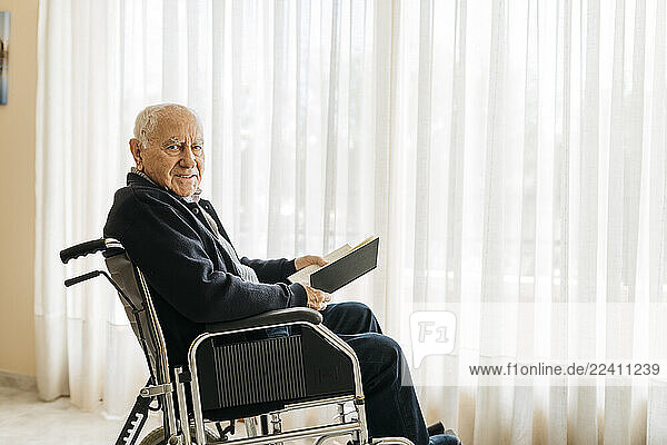 Portrait of smiling senior man sitting in wheelchair with a book
