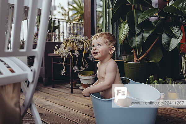 Baby boy sitting in baby bath on the balcony  try in to get up