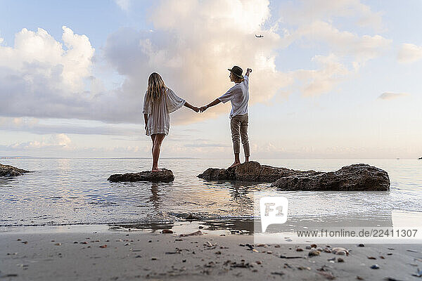 Back view of young couple standing on rocks in front of the sea  Ibiza  Balearic Islands  Spain