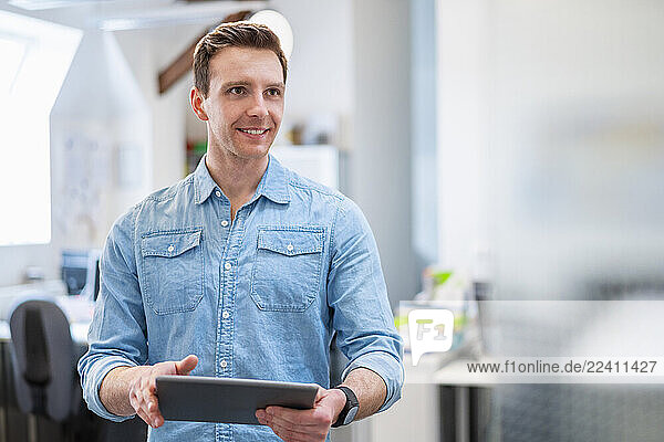 Young man in office holding a tablet and smiling