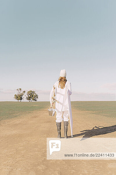 Young woman carrying easel and empty canvas on dry field