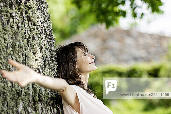 Smiling brunette woman leaning against a tree trunk