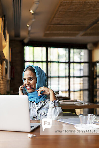 Businesswoman wearing turquoise hijab in a cafe and working with her laptop  on the phone