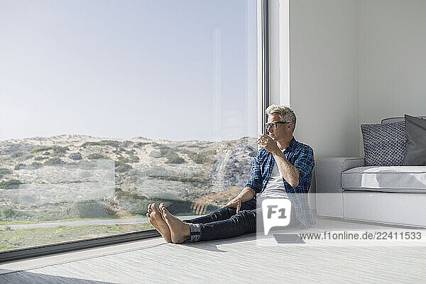 Casual businessman sitting in front of window in modern home with tablet